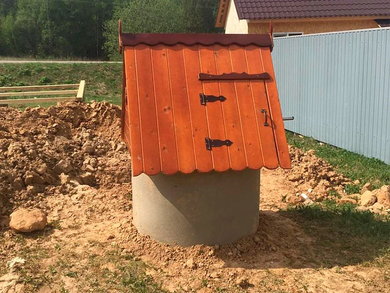 Колодец с красным деревянным домиком у забора